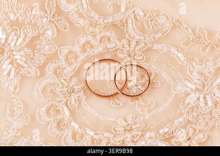 Two wedding rings sit elegantly on a delicate lace fabric, symbolizing love and commitment. The intricate lace pattern highlights the rings' beauty, p Stock Photo