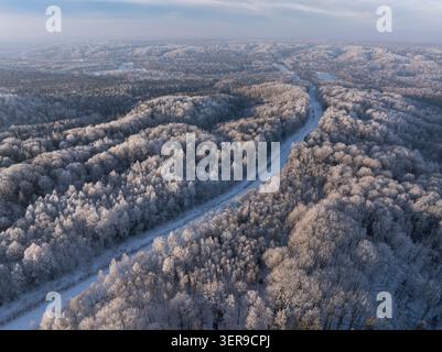 Aerial winter panorama of a winding snow-covered forest road through frost-covered woodland in Latvia Stock Photo