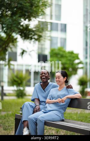 Diverse nurses laughing, talking on outdoor hospital break Stock Photo