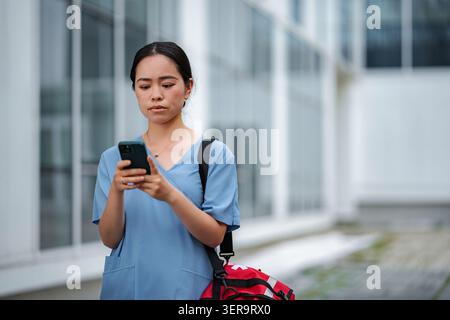 Female healthcare worker checking phone messages or medical app outdoors Stock Photo