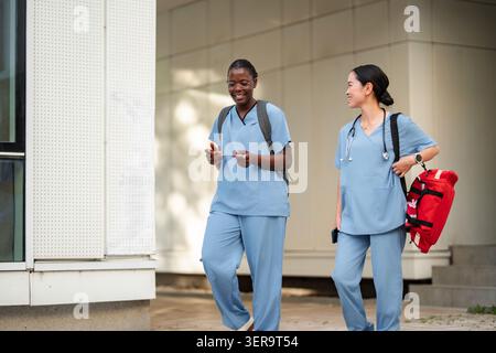 Diverse medical students walking and talking outdoors on campus Stock Photo