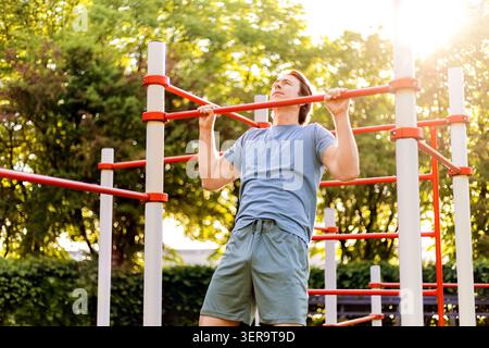 Man doing pullups on outdoor calisthenics bars during a fitness workout in a sunny park. Athlete training bodyweight exercise. High quality photo Stock Photo