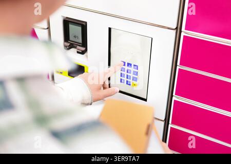 Close up of a hand entering a pin code on a parcel locker touchscreen terminal. Concept of e-commerce online shopping delivery service and package pic Stock Photo