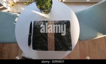 Black Parcel Wrapped in Plastic and Tape on a White Table Stock Photo