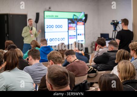 Business presentation at tech conference, speaker presents slides to attentive audience while camera records, networking and learning atmosphere. Stock Photo