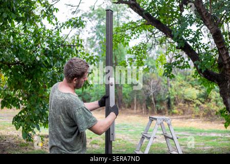 A man checks the vertical alignment of a metal fence post with a spirit level. home improvement, backyard construction, level measurement. Stock Photo