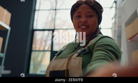 African American warehouse employee using selfie smartphone camera to participate in online videocall with management executives, worker in teleconference meeting with distribution center managers Stock Photo