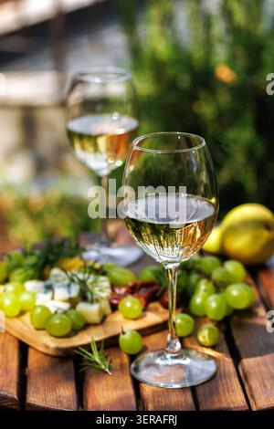 Two Glasses of White Wine with Grapes and Cheese in Garden Setting Stock Photo