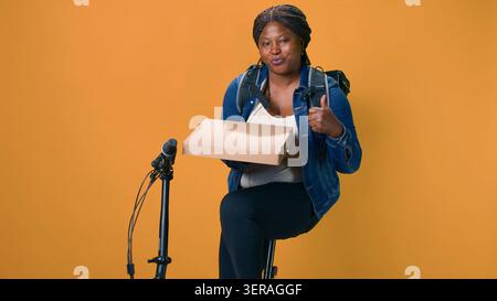 Friendly courier on bicycle carrying package from restaurant for timely reliable courier service. Black woman holding pizza box and giving thumbs up ensuring fresh sustainable food delivery. Stock Photo