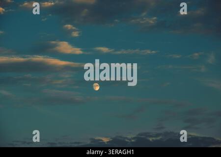 Clouds drift in sky as moon shines bright during evening hours in tranquil scene. sky shows dark blue and gray clouds as a full moon hangs in sky. eve Stock Photo