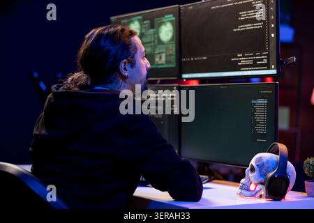 Hacker in secret hideout coding malware designed to exploit network backdoors. Rogue software developer bypassing security measures such as logins and password protections. Stock Photo