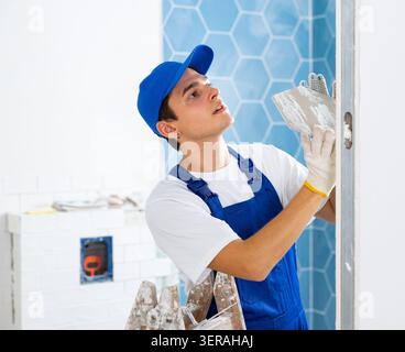 Young contractor laying tiles on walls during indoor renovation works Stock Photo