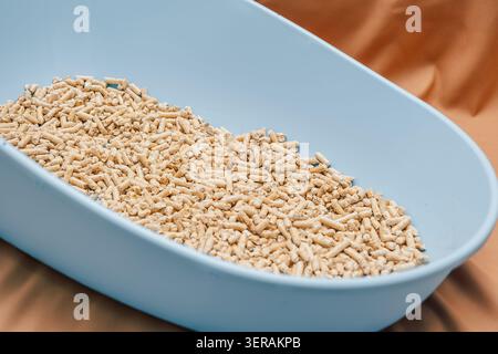 Wood pellets are held in hand above a larger pile of wood pellets in storage area. blue plastic litter box sits on a brown surface filled with wood pe Stock Photo