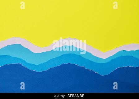 Layers of torn paper in various shades of blue and white, arranged to evoke rolling ocean waves. on vibrant yellow background. Stock Photo