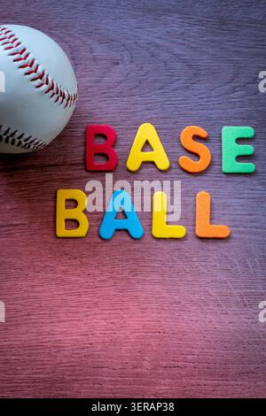 Baseball ball resting on a wooden surface with colorful letters arranged below it Stock Photo