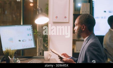 Employees working together on finishing project before impending deadline, auditing financial payroll reports in office during nightshift. Stock Photo