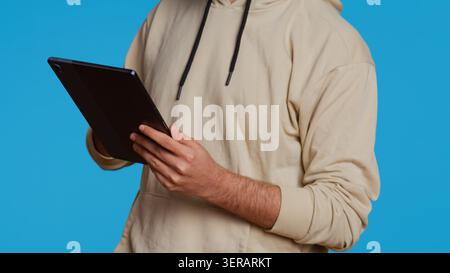 Arab guy using tablet to scroll on online websites, looking for something on the internet and using social media apps. Modern person working with touchscreen device in studio. Camera 2. Stock Photo