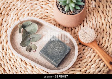 Natural charcoal soap with eucalyptus, body brush and succulent on woven mat. Eco skincare and wellness concept. Top view, flat lay. Stock Photo