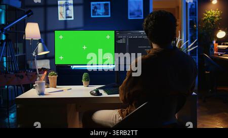 Self employed man doing IT support job from apartment personal office, coding on green screen PC, software developer writing lines of code on mockup computer at home. Stock Photo