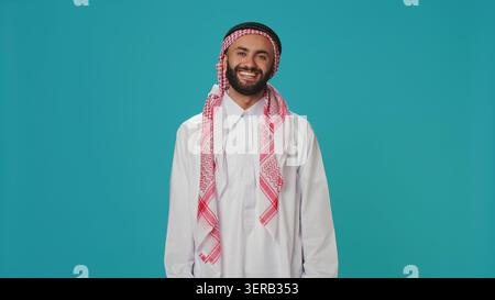 Muslim guy nodding in studio shot, saying yes and expressing his approval, arab person in traditional clothes showing support about something, middle eastern man doing positivity and agreement sign. Stock Photo
