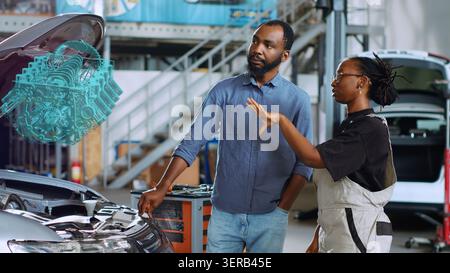 Licensed engineer in repair shop using holographic augmented reality to show woman defective components inside car. Stock Photo