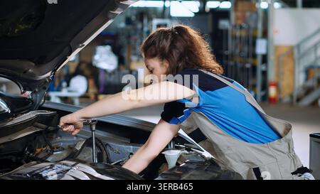 Precise mechanic in garage using torque wrench to tighten screws inside opened up vehicle after changing oil, auto repair shop employee doing checkup on car, cleaning leftover mess. Stock Photo