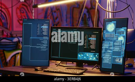 High-tech computer systems running malicious code in messy empty criminals hideaway, virus script running on PC monitors in empty neon lit warehouse used by hackers. Stock Photo