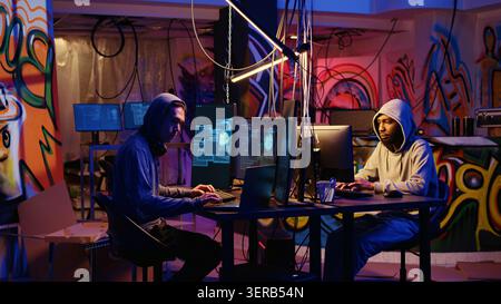 Teamworking hackers in graffiti sprayed hideaway targeting vulnerable unpatched connections, having burst of joy after getting past digital devices security and stealing valuable sensitive data. Stock Photo
