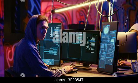 Rogue programmer in graffiti sprayed hideaway targeting vulnerable unpatched connections, focused on getting past digital devices security and stealing valuable sensitive data. Stock Photo