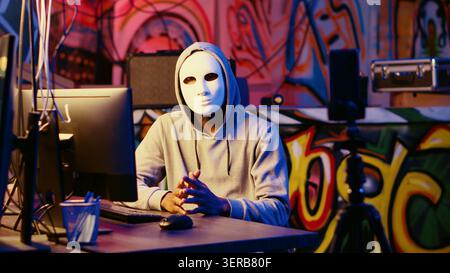 Anonymous masked dissident hacker filming anti government message, fighting against propaganda, hooded social justice crusader using smartphone to record threatening video. Stock Photo