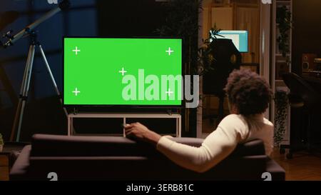 Person using chroma key video projector to binge series on subscription based streaming services, cord cutter relaxing on couch, enjoying video on demand shows on mockup smart TV. Stock Photo