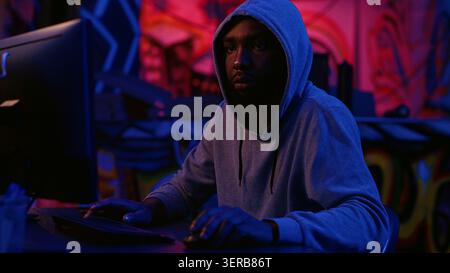 Hacker in secret dark room writing lines of code on computer, developing virus that get past security systems, evil developer uses PC in hidden bunker, running hacking script. Stock Photo