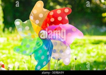 Colorful rainbow pinwheel wind spinner with polka dot pattern on a blurred green grass background Stock Photo