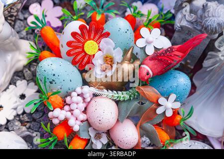 Easter wreath with colorful speckled eggs artificial red flower red bird decorative carrots and golden bunny close up Stock Photo