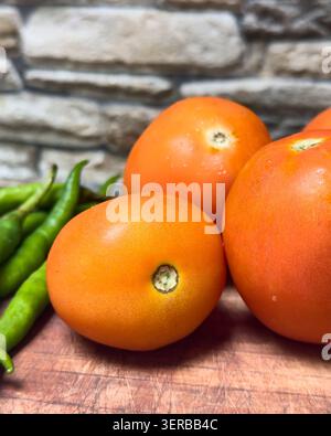 fresh tomatoes and green chilies on wooden board with wall background, ripe red vegetables and spicy raw peppers, close-up soft focus view Stock Photo