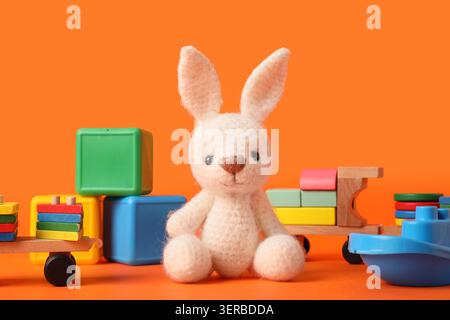 Adorable white knitted bunny toy with colorful wooden and plastic blocks on bright orange background, childhood play and early learning development Stock Photo