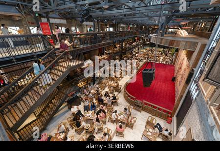 Multi-Level Indoor Teahouse With Crowded Dining Area and Red Performance Stage in Urban Food Hall. Stock Photo