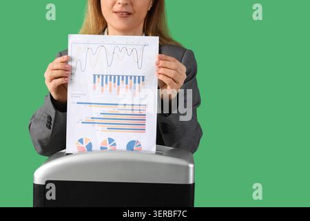 Adult woman destroying documents using shredder on green background, closeup Stock Photo