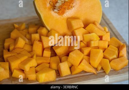 Freshly chopped pumpkin cubes on a wooden cutting board. Healthy autumn vegetable, ready for cooking, roasting, or making soup. Organic ingredient for Stock Photo