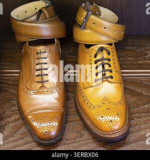 Brown and tan full grain leather shoes with belts on wooden display in men shoes boutique store Stock Photo