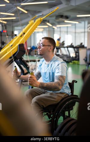 Concentrated disabled man in wheelchair working on spinal injury rehabilitation in sports center. Stock Photo