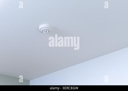 A white smoke and fire detector mounted on a clean white ceiling corner in a Japanese residential space. A documentation shot for home safety and new construction inspection. Stock Photo