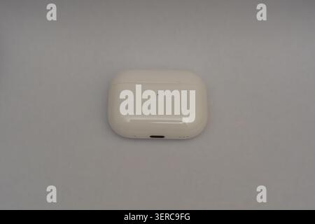 White charging case rests on plain surface. Minimalist design, clean and simple. Soft lighting highlights smooth contours. Subtle shadow adds depth to Stock Photo