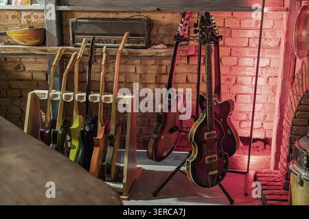 Guitars and bass displayed prominently on wooden stand, showcasing variety of wood finishes and shapes, featuring vintage-style amplifier on shelf abo Stock Photo