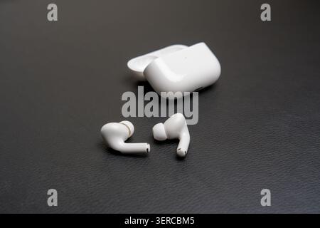 White earbuds rest beside open charging case. Dark textured surface provides clean contrast. Minimalist product shot for tech or lifestyle use. Modern Stock Photo