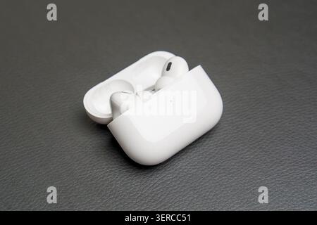 White earbuds rest in open charging case. Case sits on textured gray surface. Clean, minimalist product photography. Modern electronics design showcas Stock Photo