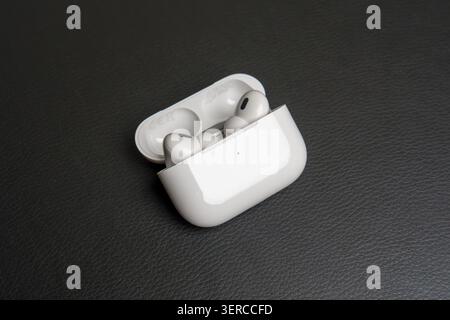 White earbuds rest in open charging case. Case sits on dark textured surface. Modern design features smooth edges. Clean aesthetic highlights minimali Stock Photo