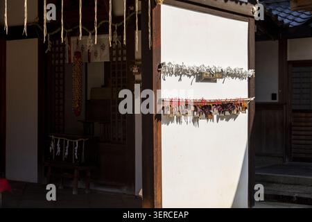 View of traditional wooden prayer plaques and tied paper fortunes on a white wall at a Japanese shrine in Nara, Nara, Japan. Stock Photo
