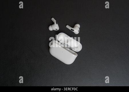 White earbuds rest beside open charging case. Surface has fine, dark textured grain. Device shows clean, minimalist design. Earpieces sit open, ready Stock Photo