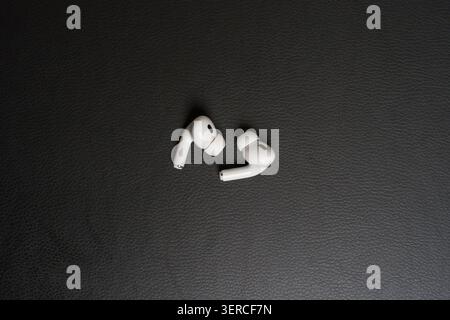 White earbuds rest on dark textured surface. Simple, clean design emphasizes minimalist style. Soft curves contrast with matte background texture. Pro Stock Photo